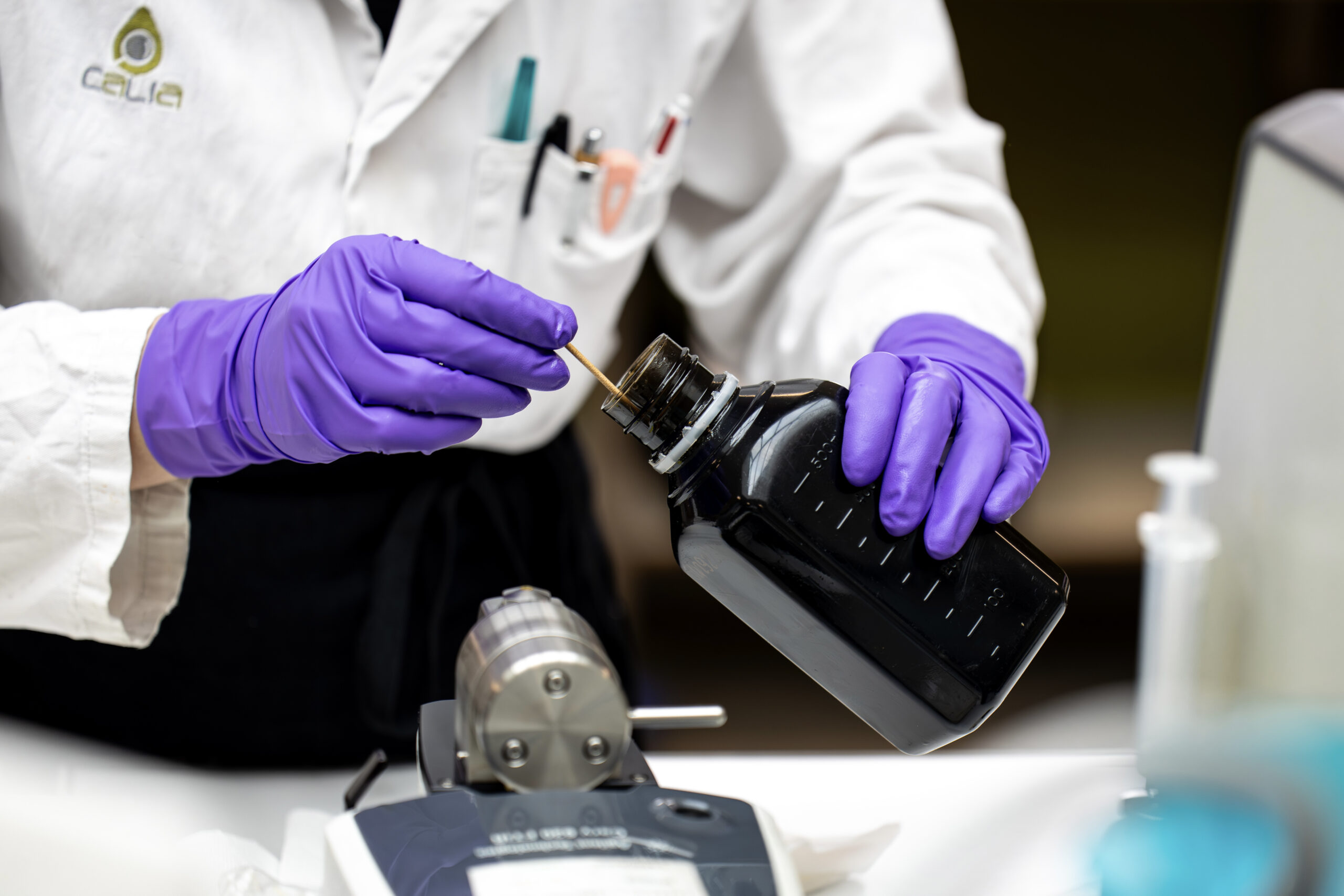 Technicienne réalisant une analyse en laboratoire avec un flacon de liquide noir
